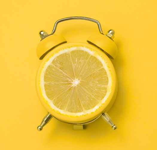 Das Bild zeigt einen Wecker mit einer Zitrone als Ziffernblatt